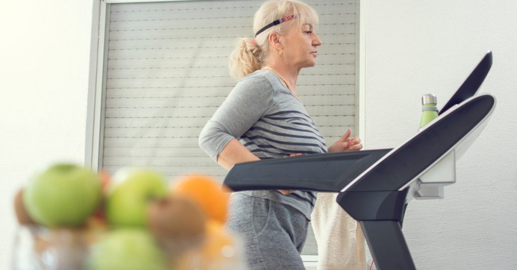 Elderly lady walking on the treadmill in her home.